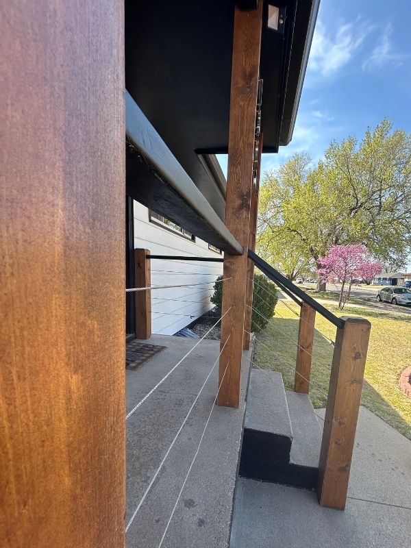 Side view of front porch construction project featuring natural wood posts, black handrails, and connecting cable wire.