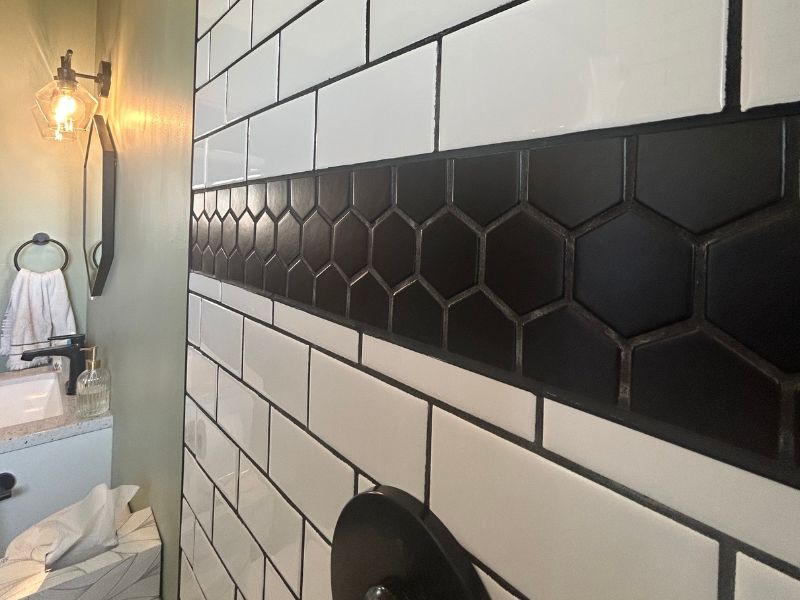 Detail photo of shower tile in a bathroom remodel project. White subway tile accented by a strip of black hexagon shaped tile.