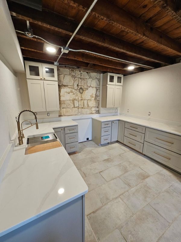 Remodeled kitchen complete with grey shaker style cabinets, exposed wood ceiling, stained concrete flooring, and gold accents.