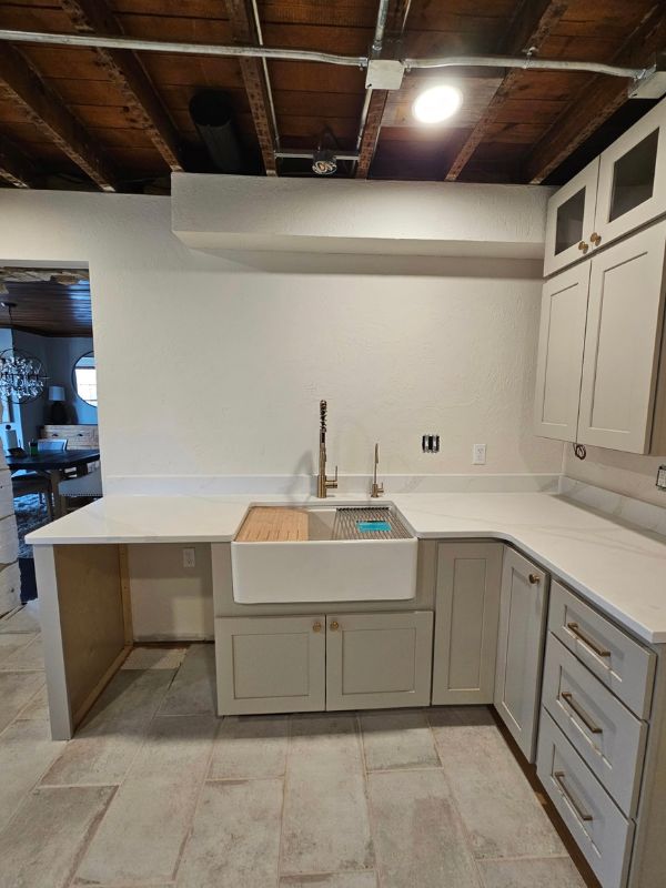 Large, white farmhouse sink with a gold fixture in a renovated kitchen.