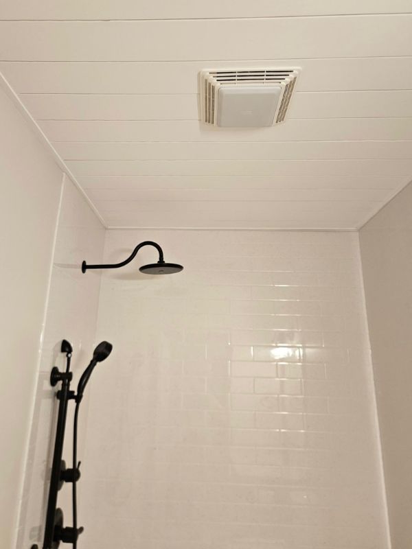 Detailed shiplap ceiling accents a white Onyx shower wall in a remodeled bathroom.