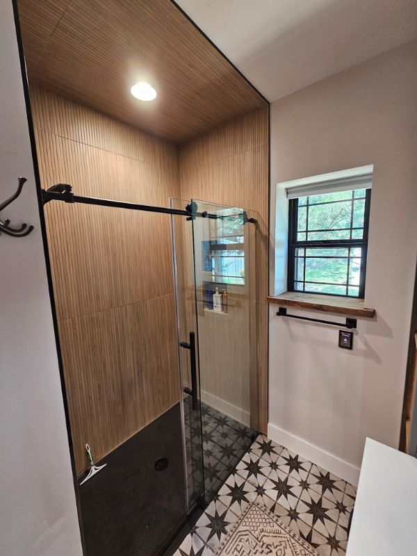 Bathroom addition in Hays, Kansas featuring vertical, tan tile, a black shower base, and patterned flooring.